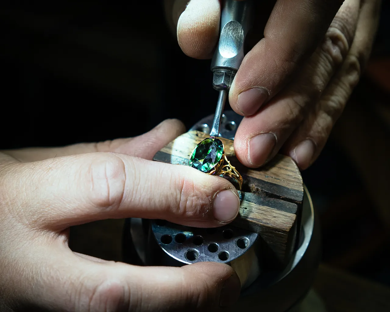 A jeweler at CJD Fine Jewelry setting a large oval emerald into a custom gold ring. A jeweler at CJD Fine Jewelry setting a large oval emerald into a custom gold ring.