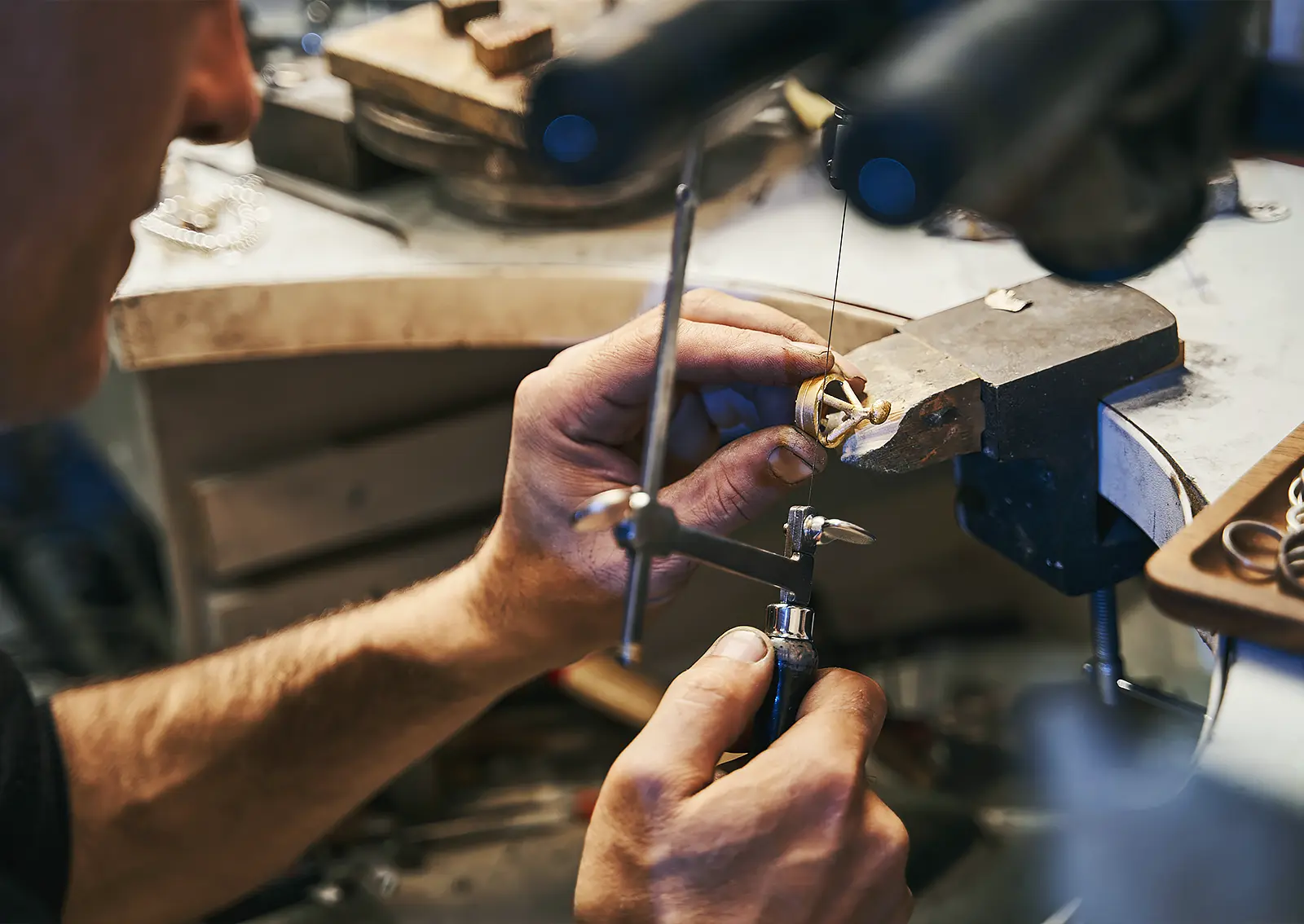 A jeweler sits at a workbench, creating a custom piece of jewelry from yellow gold.