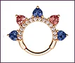 Custom gold piercing ring with heart-cut sapphires, rubies, and clear diamonds.